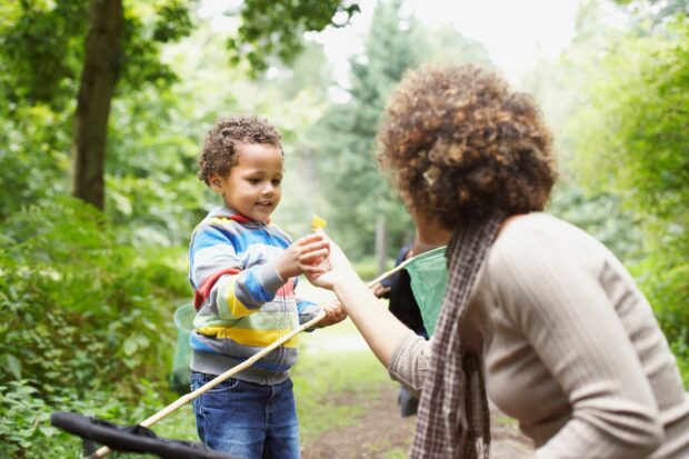 A mother gives a leave to her young child, who is holding a small rake for working in the garden