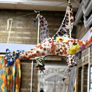 Photo shows a hand made sea horse from the school children, it hangs from the ceiling within the school. It is brightly coloured with orange and yellow dots 