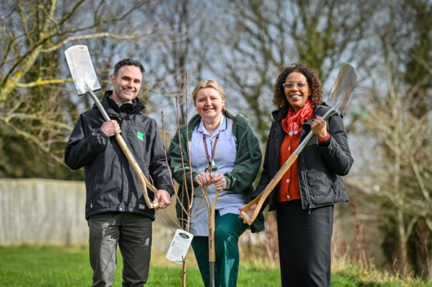 Image shows Natural England’s Chief Operating Officer, Oliver Harmar, Senior Occupational Health Therapist, Tracy Metcalf and the Care Trust’s Chief Executive, Therese Patten. They stand together on a NHS site, all hold gardening tools, ready to get to work.