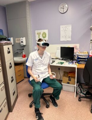 An occupational therapy student engaged in virtual reality nature, she sits with a VR headset on, within an office at a NHS site. 