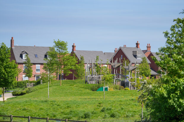 Image shows a neighbourhood that has implemented good GI. A green park sits in front of red bricked houses, a clear blue sky hangs overhead. The trees and grass are lush and vibrant