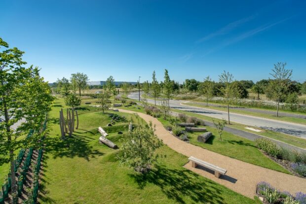 Image shows a neighbourhood that has implemented good GI. A green park with a pathway runs through it, a clear blue sky hangs overhead. The trees and grass are lush and vibrant