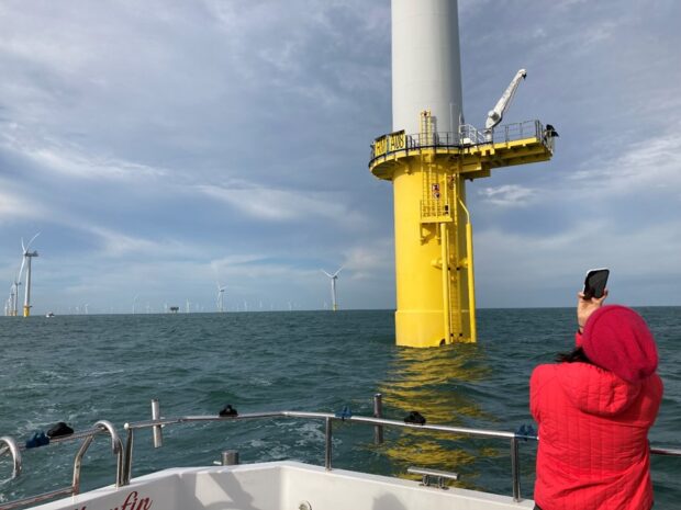 A person on a boat in the sea taking a picture of a large wind turbine, which is part of an offshore wind farm in the North Sea