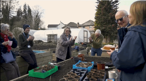 Image of people smiling and sharing cake in an allotment.
