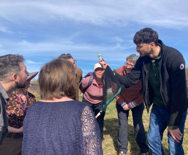 Group of people gathered in a circle, with one man holding a sample collection tube up. Everyone is looking at the tube and smiling.