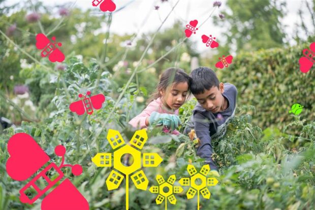 Two children, one boy and one girl, wearing gardening gloves and reaching into a garden bed with interest.