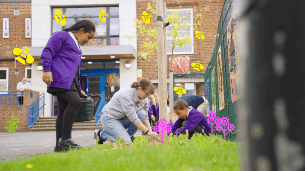 Children in school uniforms help with planting outside of a school. An adult and child are kneeling in the foreground, digging at the base of a young tree, while another child stands with a watering can.