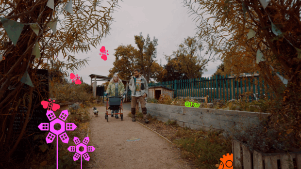 A woman with a mobility aid is walking a small dog, alongside a man in outdoors gear. They are walking on a path with foliage and planters on either side.