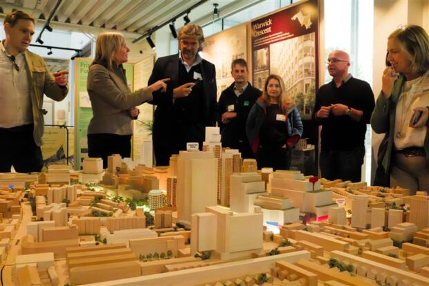 A group of people in discussion around a model of a housing development on a table.