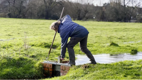A man operating a sluice in water meadow