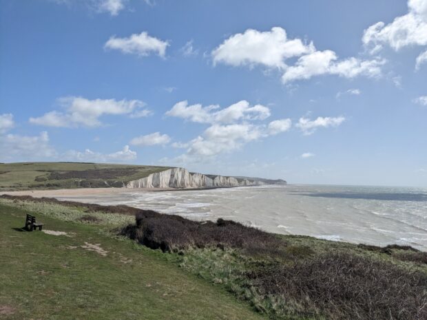 Wide shot of the seven sisters cliffs in the sun, with the beach and the sea and surrounding grassland.