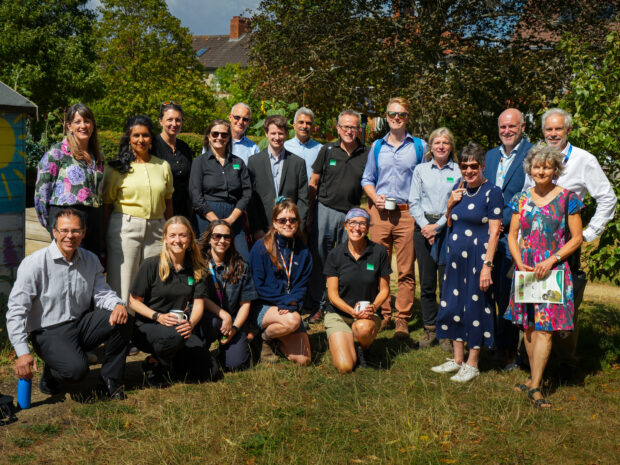 A group of 19 people together posing for a photograph outdoors in the sun.